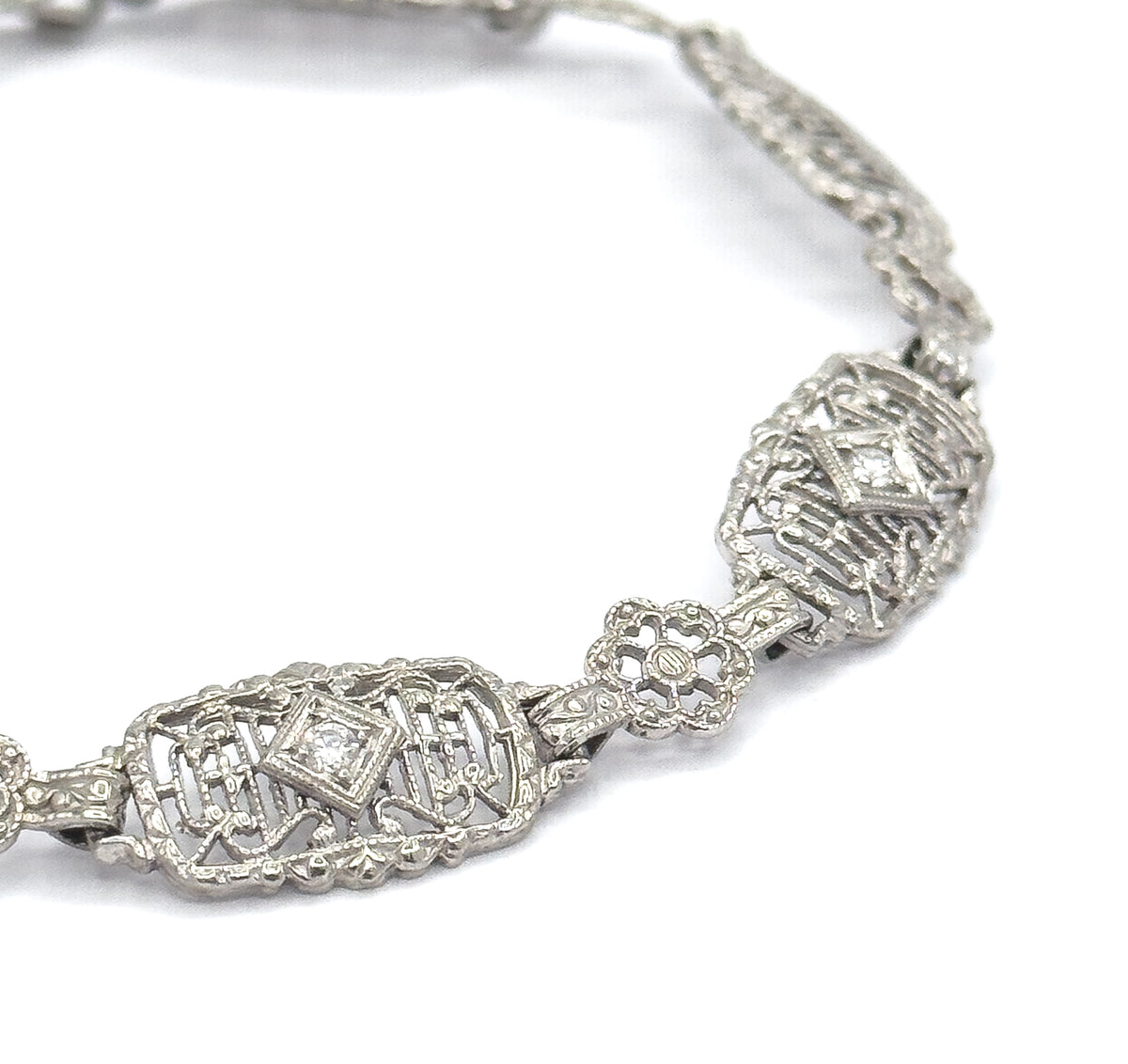 Close angled crop along the curve, two diamond-set oval links and the pierced four-petal link between them filling the frame while the rest of the chain recedes behind.