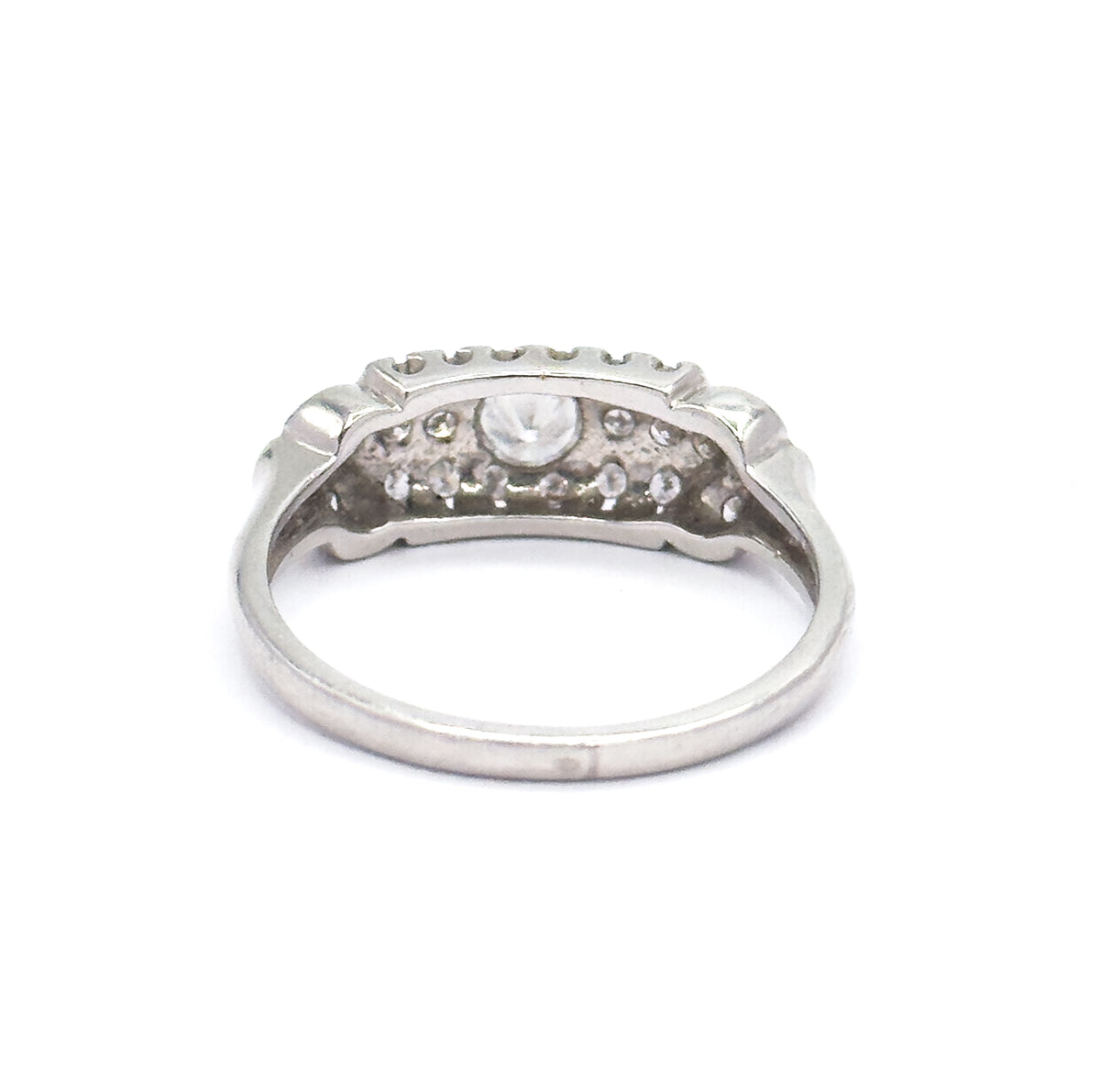Rear view against white with the shank curving toward the viewer, the underside of the head open so the backs of the centre stone and surrounding pavé show between the scalloped edges.