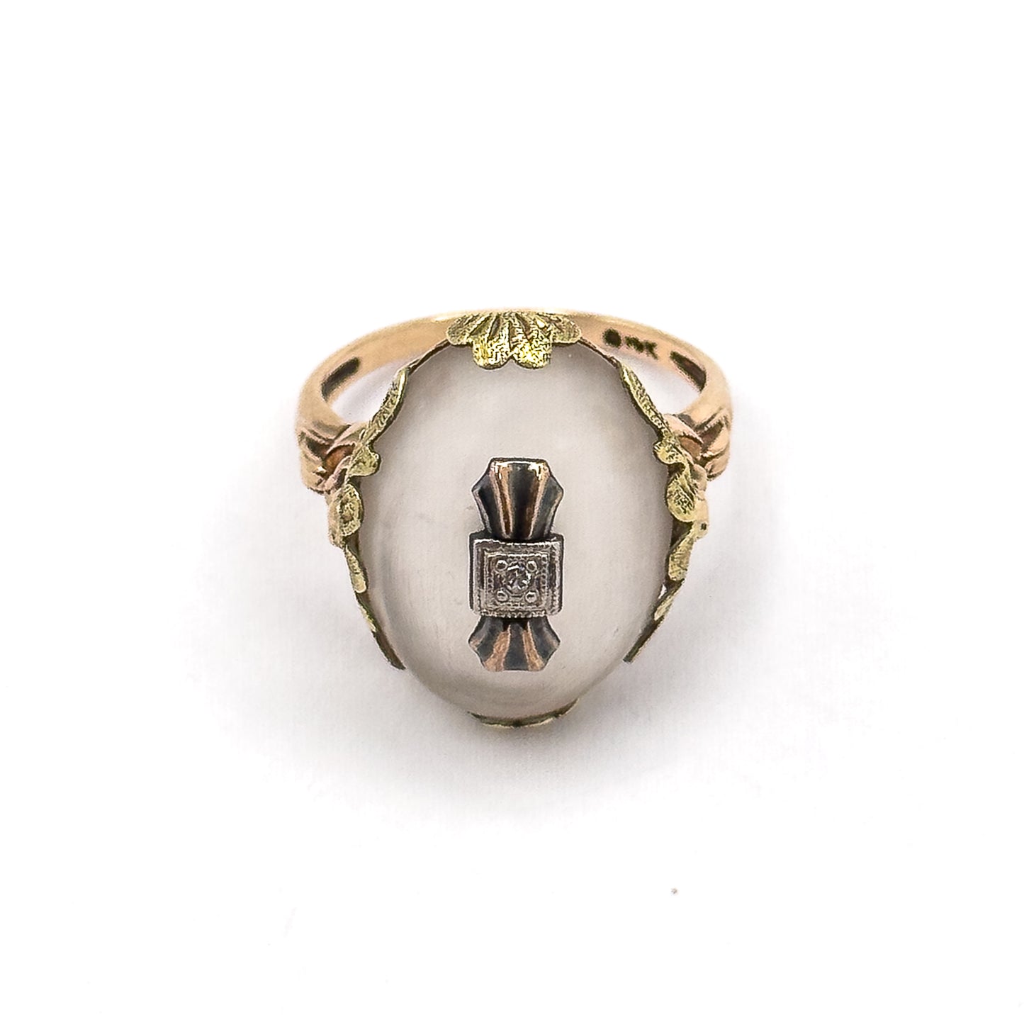 Face-on from above with the ring standing upright, showing the full oval cabochon, the central white metal plaque with its diamond, and leafy galleries curving down both sides to the shank.