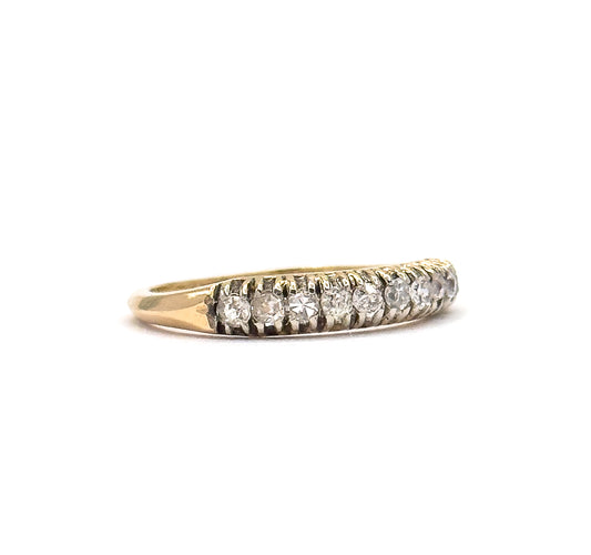 Side profile against a plain white background, the band lying so the row of round diamonds and their ridged prongs runs along the top while the yellow gold shank curves away below.