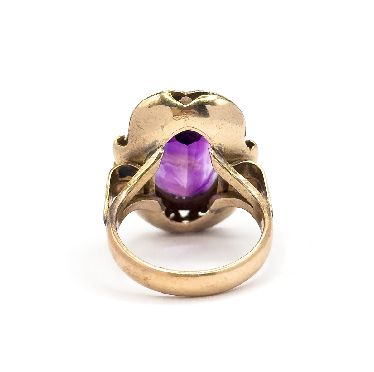 Looking straight into the back of the setting, the amethyst's underside shows pale purple between the gallery's open scrolls, with the smooth yellow gold shank curving below toward the viewer.