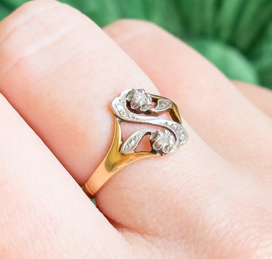 Close view on the finger from above, the two prong-set diamonds and milgrain-edged openwork of the white gold "S" face filling the frame against the yellow gold shank.