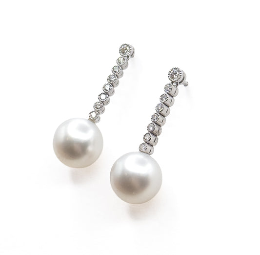 Both earrings angled side by side with the pearls lowermost, this view showing the posts projecting from the top bezel and how each bezel shrinks slightly down the diamond line.