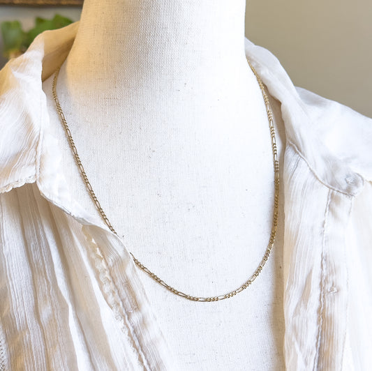 Almost the same view with slightly different angle, closer in on the chain's dip between the open collar points, where the alternating round and oval links read clearly against the pale fabric.