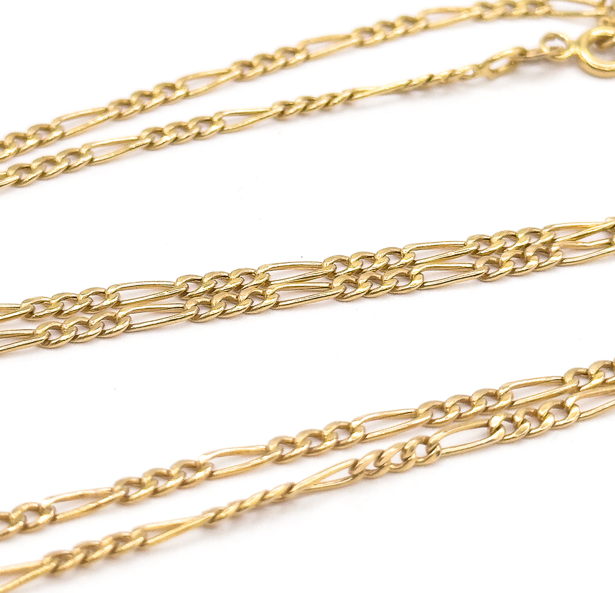 Three diagonal runs of the Figaro chain cross the frame at an angle, the polished links sharpest in the middle row while the spring ring clasp sits small and blurred at the top right corner.