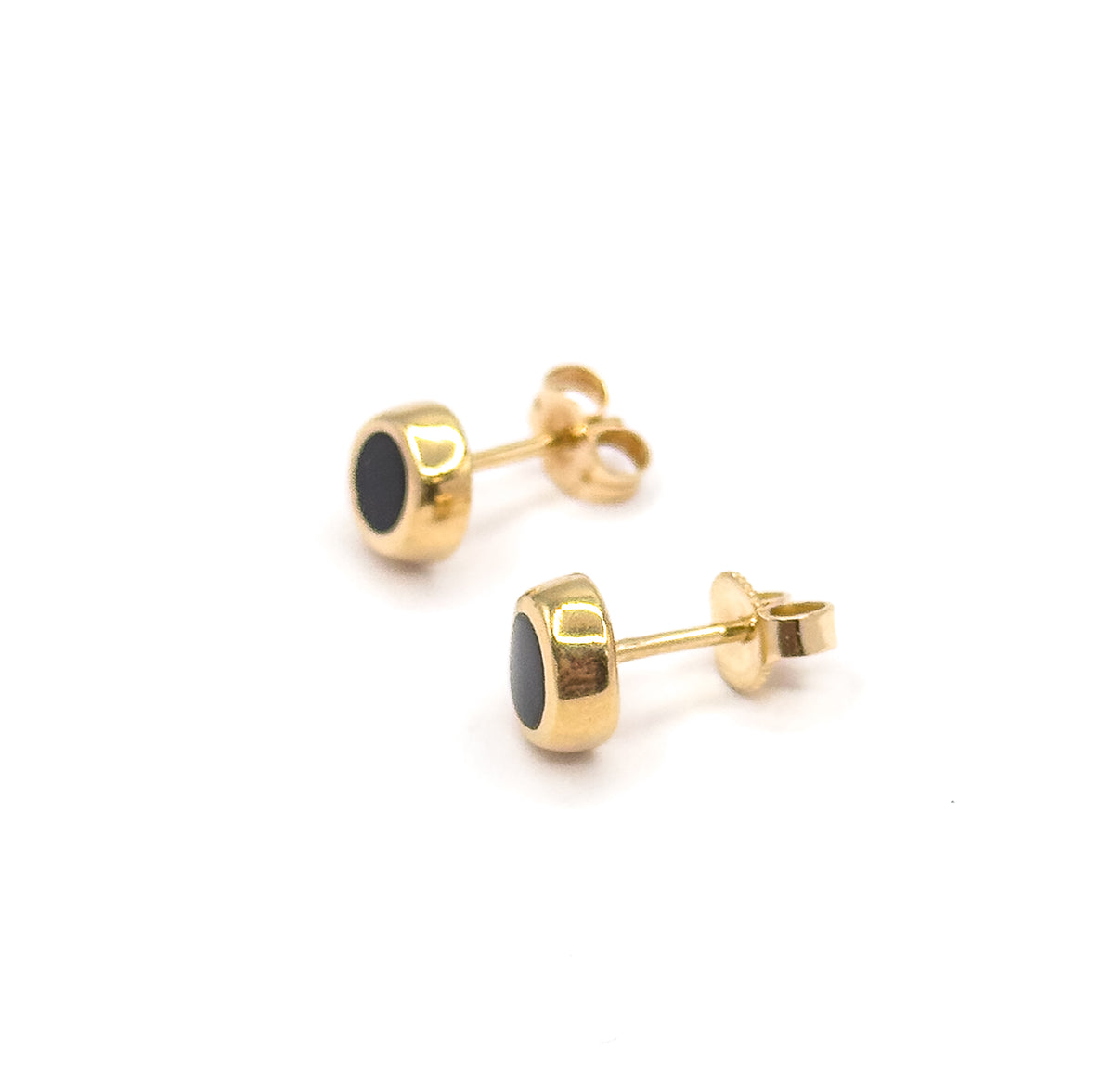 Both studs lie diagonally with posts running off to the right, showing the bezels in near profile so the black enamel appears as a narrow sliver within the yellow gold rim.