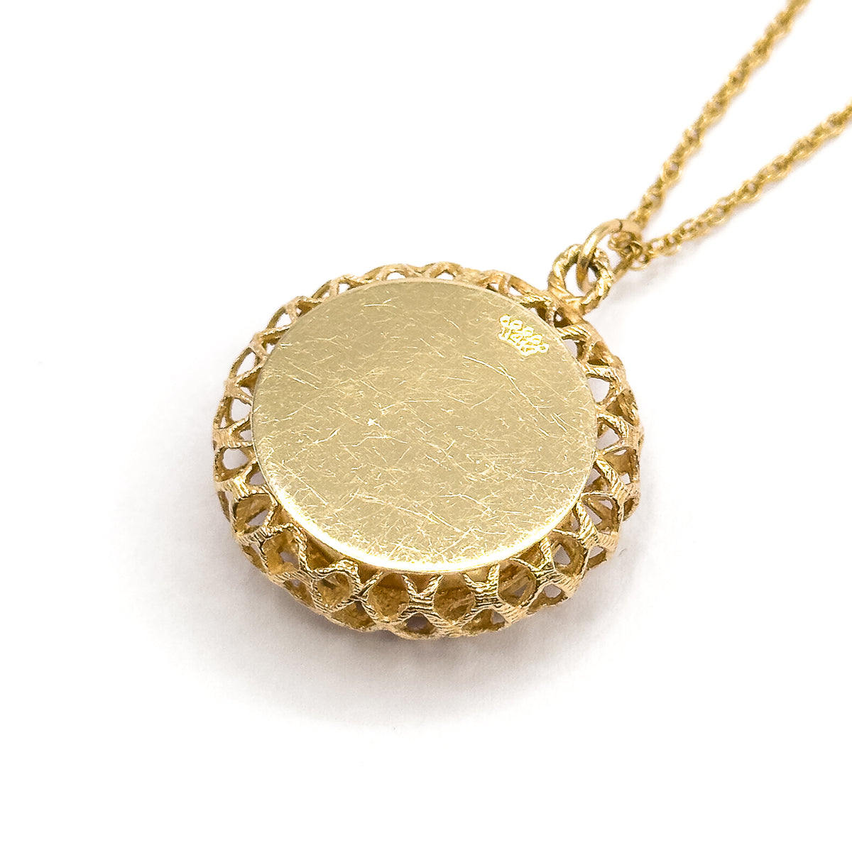 The smooth flat back of the pendant angled up on a white ground, its lattice gallery rimming the edge, a small crown stamp near the bail where the chain attaches.