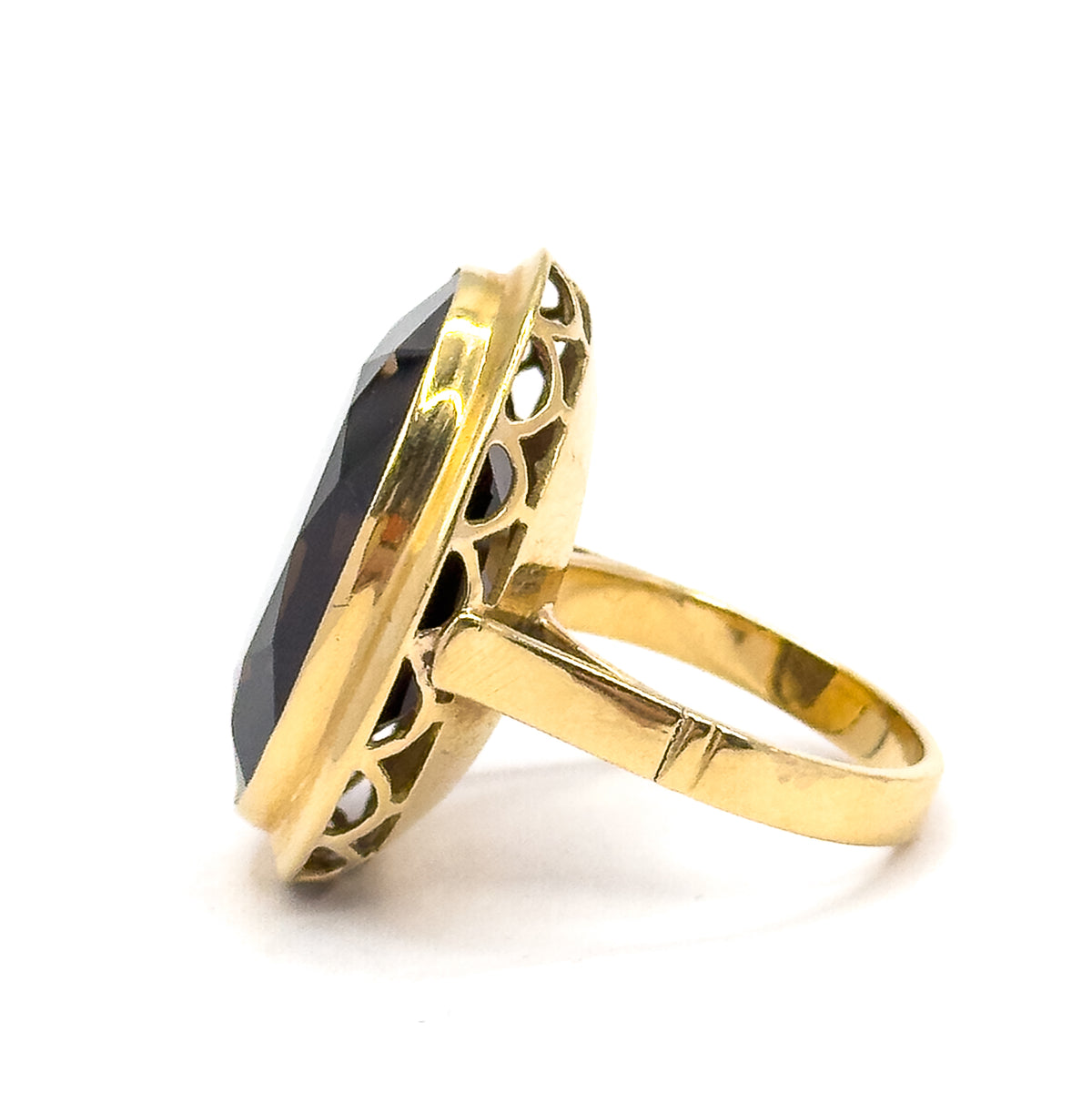 Angled from the side with the oval face tilted away from the viewer, the deep bezel wall and its faceted dark stone fill the frame while the scalloped gallery arches march back toward the shoulders.