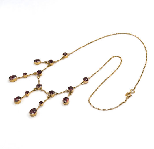 The whole necklace laid out flat on white in an open loop, the garnet festoon fringe spread at the left and the fine cable chain sweeping round to the spring ring clasp at the right.