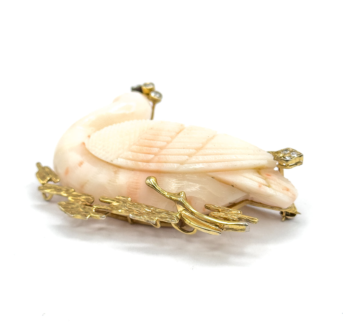 A low front-on angle with the swan's head dipped at the left, diamonds set above the head and at the right edge, and the textured gold reeds sweeping across the foreground below the coral body.