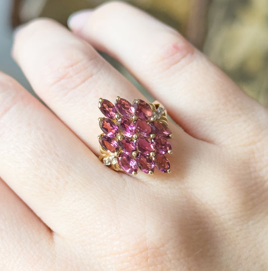 A closer look at the same hand, the purplish pink garnets filling the width of the finger and the polished yellow gold shank tapering away beneath the cluster.