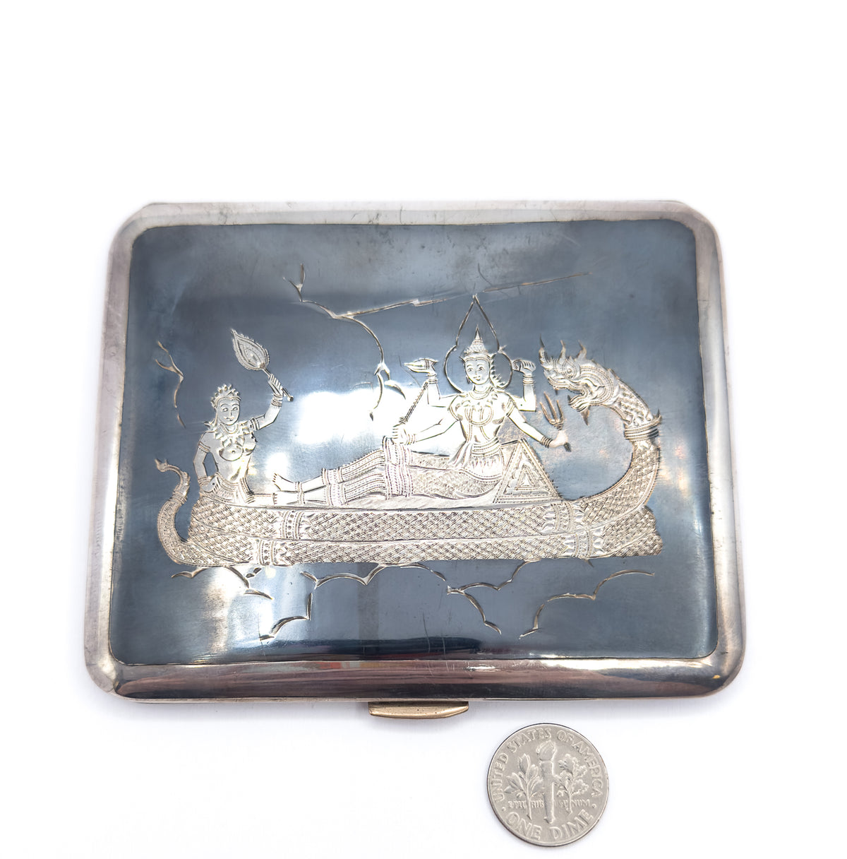Flat from above with a US dime laid beside the lower right corner for scale, the case reading roughly four dimes wide, its slate-black engraved panel framed by the bright silver rim.