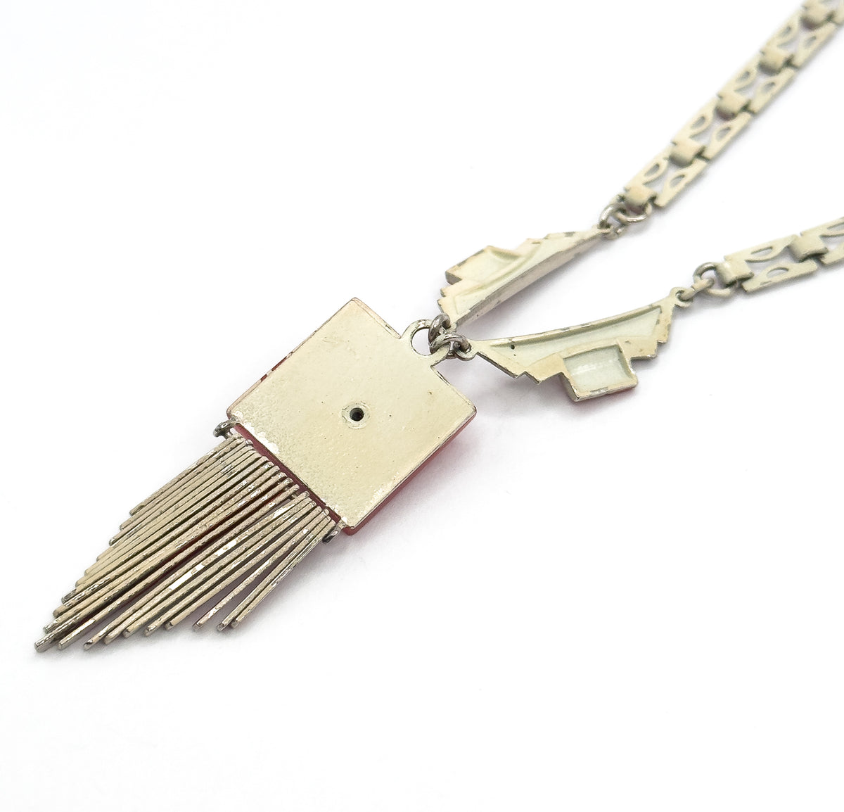 Reverse view of the square plaque with a small central hole, its straight fringe rods fanning out below while the enamelled backs of the angled shoulder links and chain run off to one side.