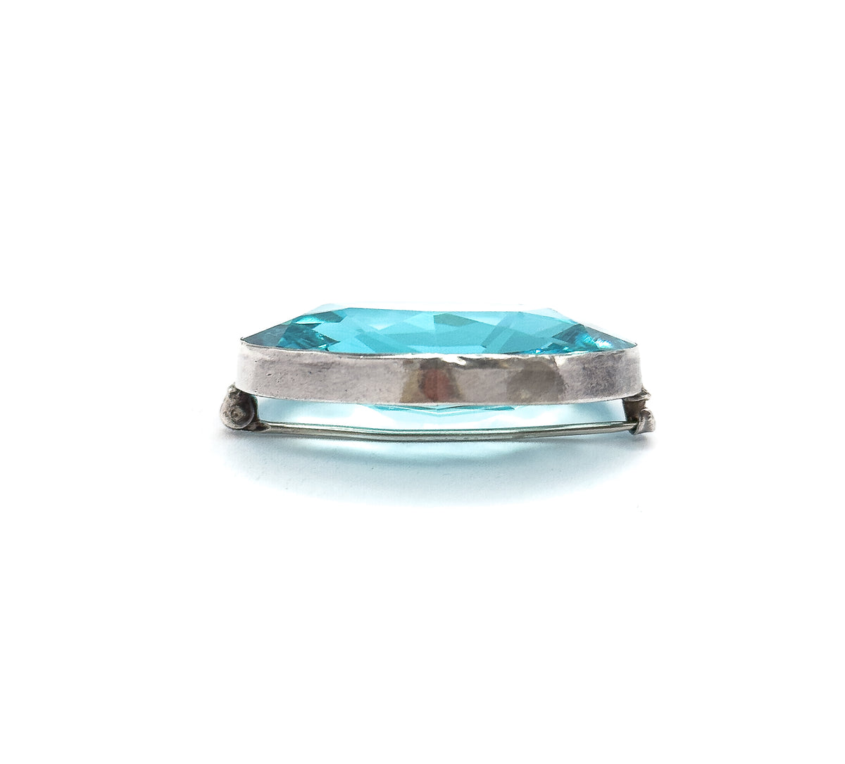 Edge-on side view on white, showing the depth of the sterling silver bezel band, the pointed pavilion of the blue paste stone below it, and the pin stem spanning between hinge and clasp.