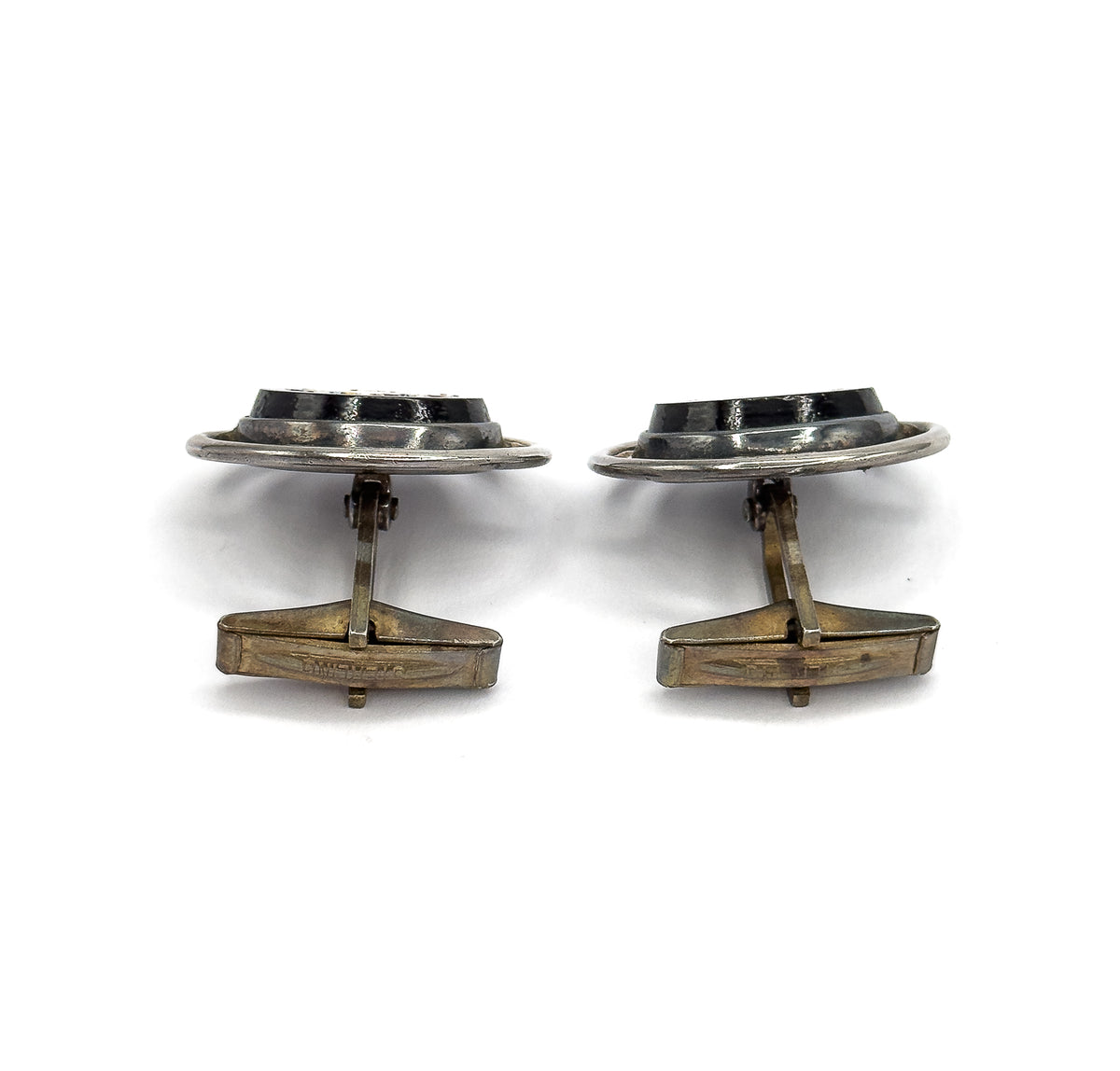 Edge-on rear view of both cufflinks side by side, showing the hinged posts and long pivoting toggle bars beneath the oval faces, with patina darkening the silver.