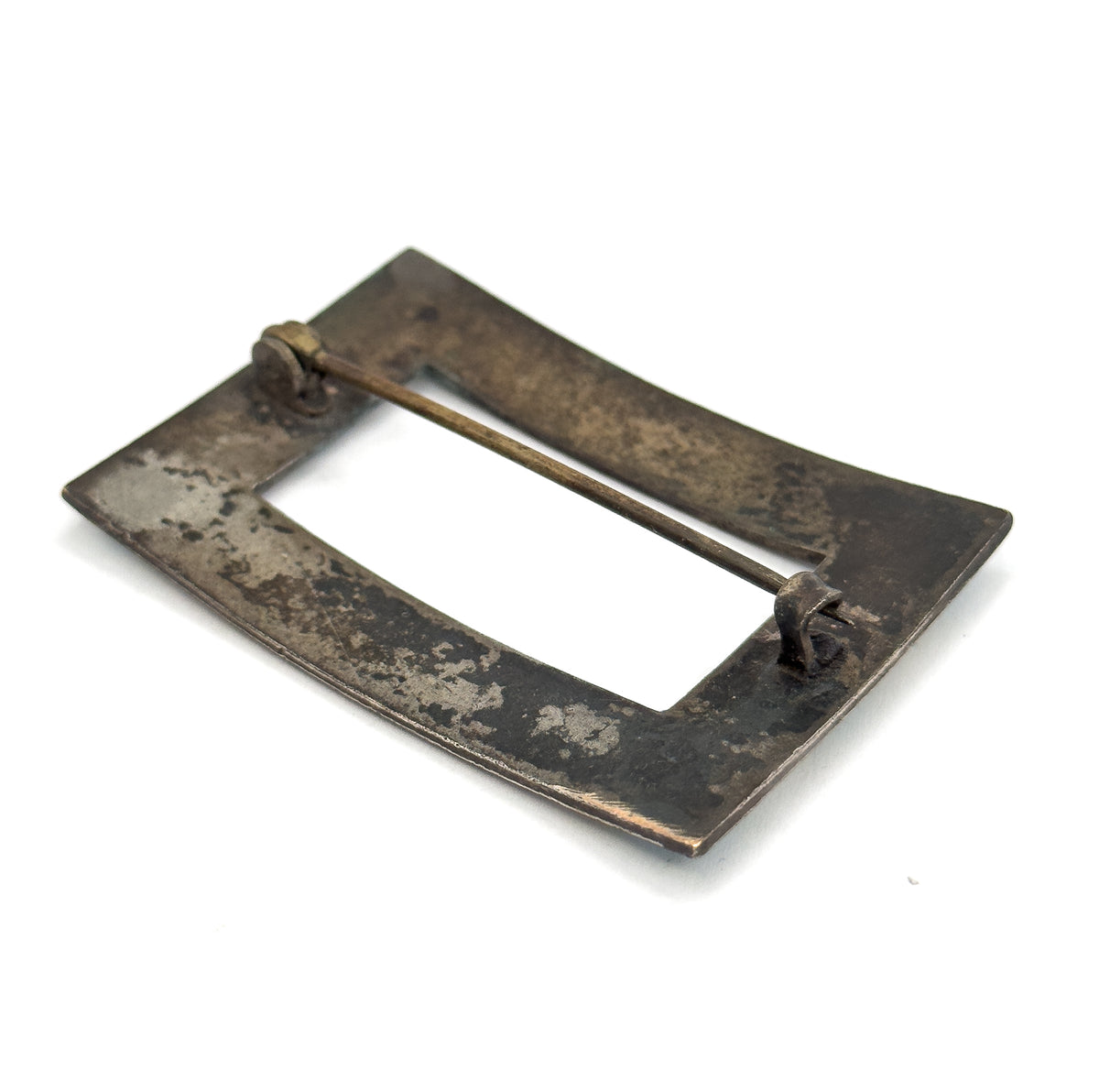 Rotated so the back lies nearly flat and diagonal, the wide underside of the frame catching the light with the hinge at upper left and the curled catch at lower right holding the pin stem.