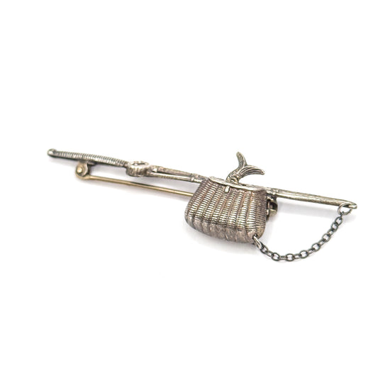 Raised three-quarter view from the pin side, the pole angled away to the rod tip at upper left, basket and fish tail at centre and the safety chain swinging in a loop below.