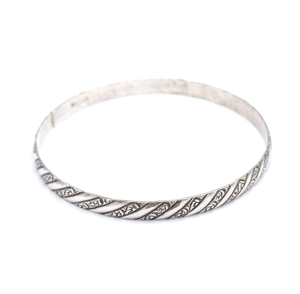 The whole bangle tilted almost flat to the camera so the full circle and its open centre are visible, repousse stripes running along the near rim and the plain band fading at the back.