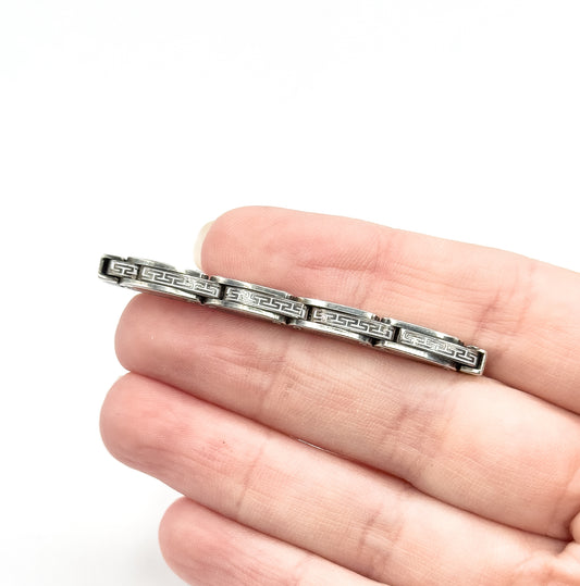 Vintage sterling silver openwork link brooch, a slim bar of geometric links with darkened patina in the recesses, shown resting across the fingers of a hand for scale.
