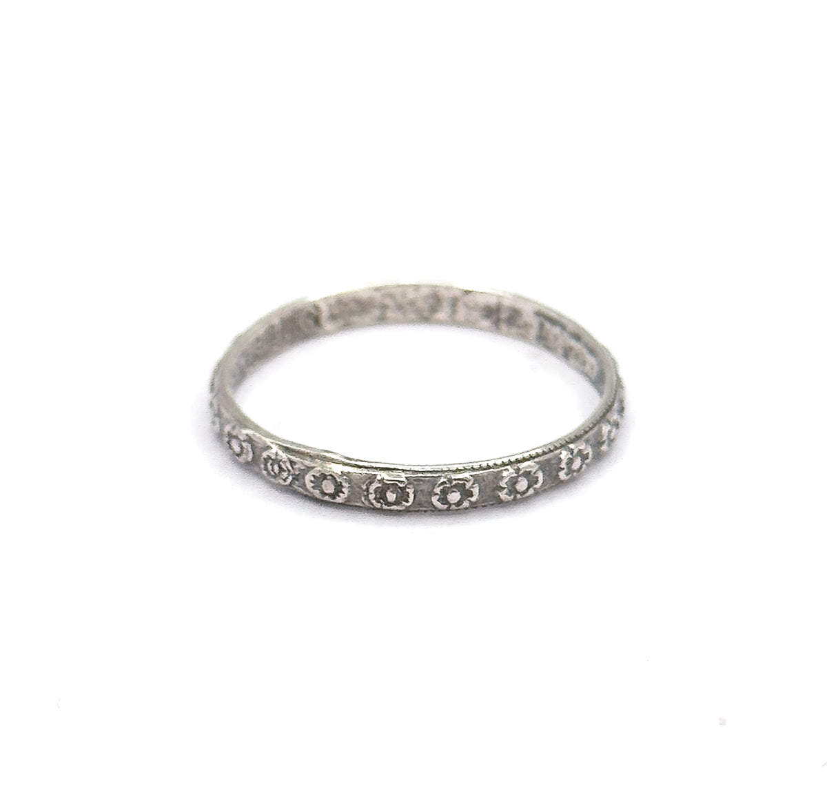 Seen from a low, near-level angle, the hoop appears as a slim ellipse so the narrow depth of the shank is clear, with the stamped flowers catching light along its lower front edge.