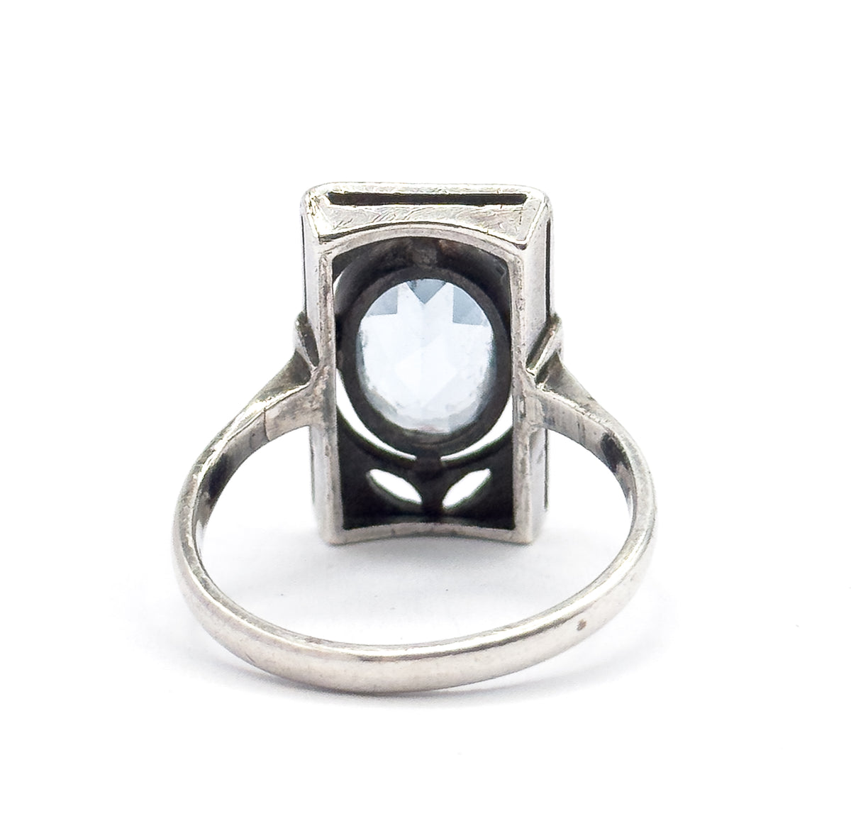 Reverse of the ring laid flat, the full circle of the slim shank framing the gallery's petal-shaped cut-outs and the open back of the bezel where the oval icy blue stone shows through.