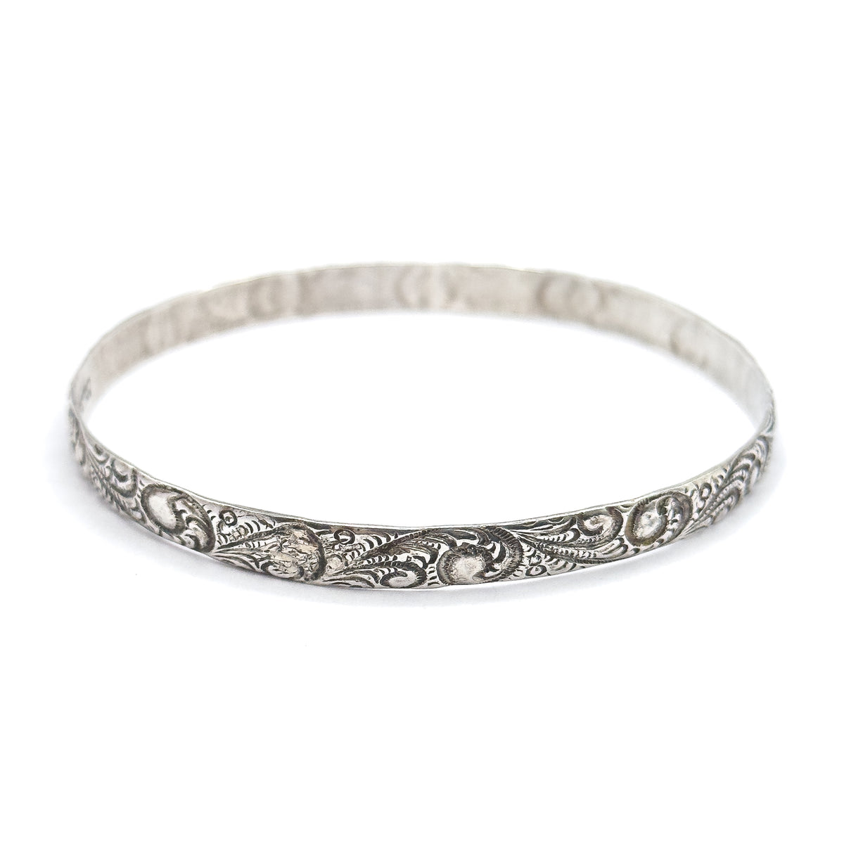The whole sterling silver bangle seen from a low angle on a plain background, the full oval standing closed and upright with scrollwork sharp across the near rim.