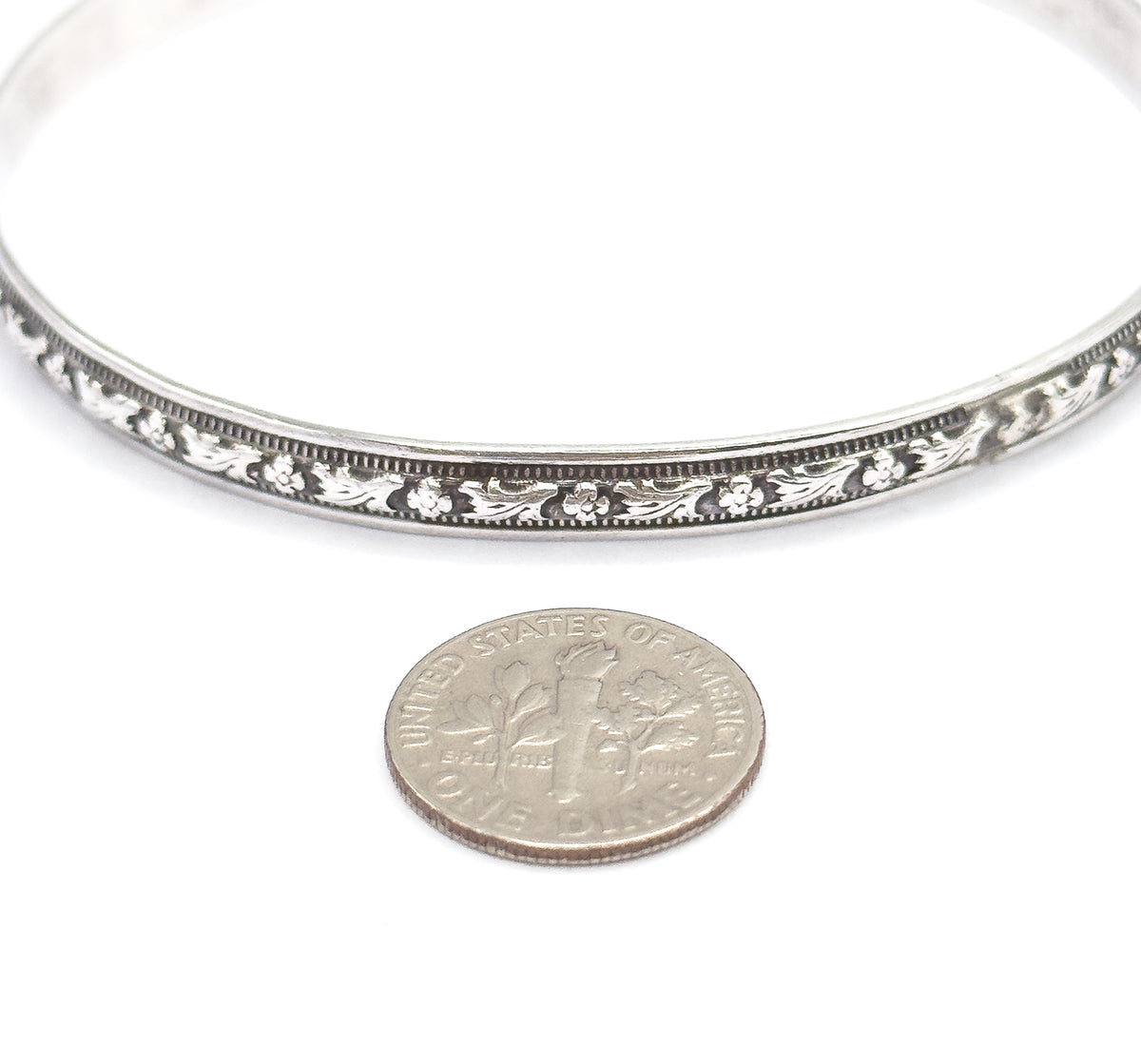 A ten-cent coin placed below the bangle gives the scale, showing the carved flower-and-leaf band and its beaded borders as only a little wider than the coin's rim.