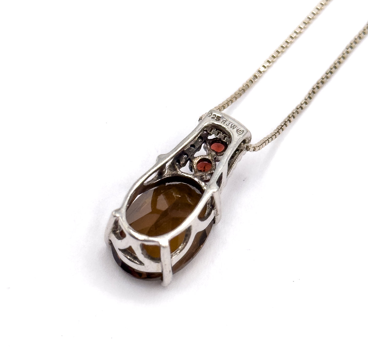 Silver pendant necklace shown from the back at an angle, the open basket setting cradling the oval quartz with two round garnets above, the box chain trailing off to the upper right.