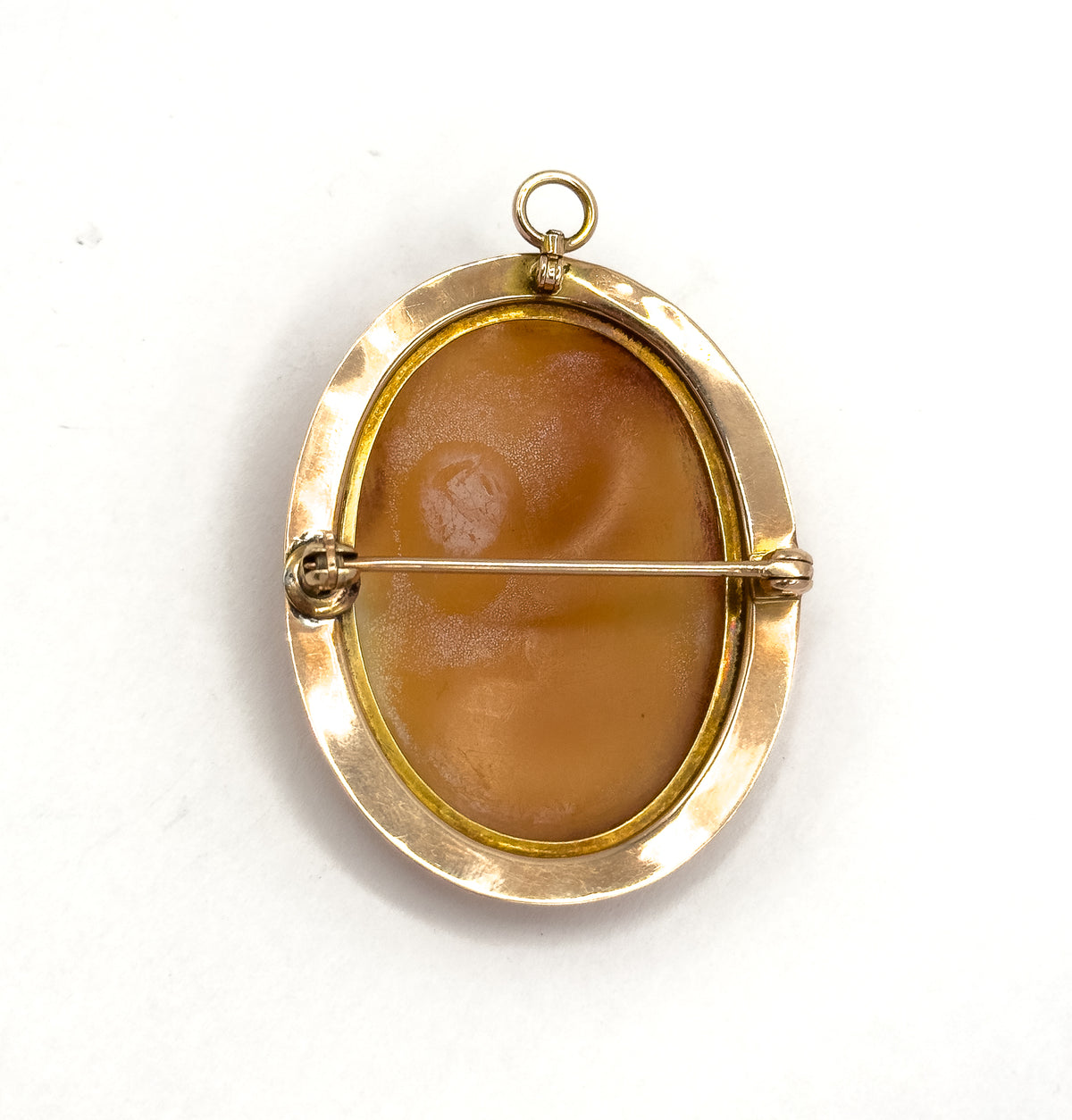Reverse view on white, the smooth tan underside of the shell set within the gold frame, with the pin stem crossing from hinge to catch and the round bail at top.