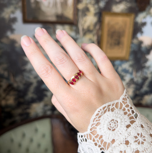 The whole hand is shown against a tapestry backdrop, the five-stone ring small and low on the ring finger, giving a sense of its scale beside the lace cuff.