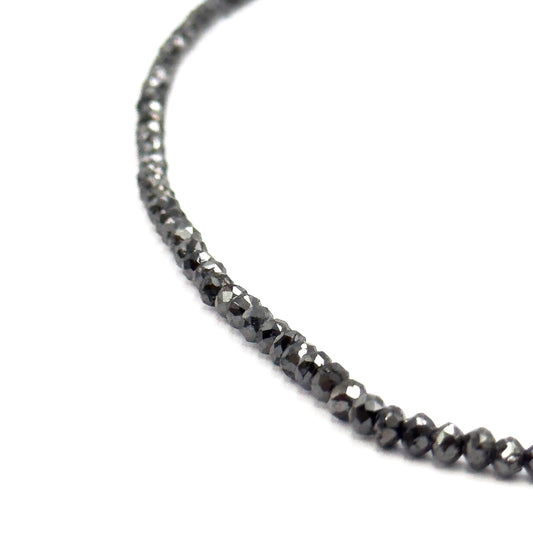 A sweeping arc of the strand curving across white, the beads tapering from tiny at the top to noticeably larger toward the bottom of the frame, showing the full graduation.