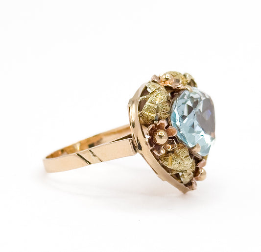 Side profile against white, showing how high the icy blue aquamarine and its leaf-and-flower halo stand above the flat tapering shank.