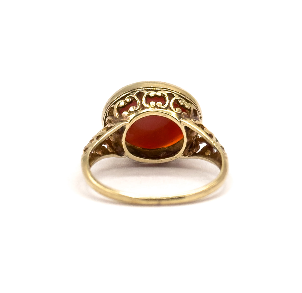 Rear view from behind the shank, looking into the open back of the setting where the coral shows through the aperture, framed by scrolled filigree and the slim band curving below.