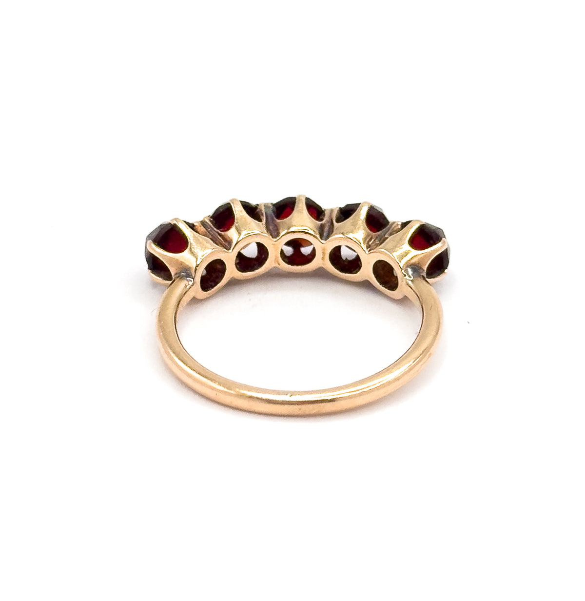 Rear view with the ring upright, the open backs of the five settings showing the flat undersides of the garnets as small red discs ringed by yellow gold collets above the plain shank.