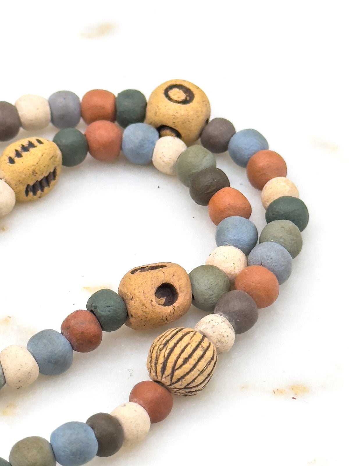 Close crop on a looped section against a white surface, showing the larger patterned beads — one with a ring motif, one with a dot, one ribbed — set among small round beads in blue, green, red and cream.