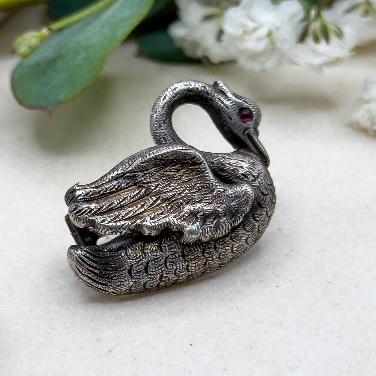 Silver swan figurine on a light surface with green leaves and white flowers in the background