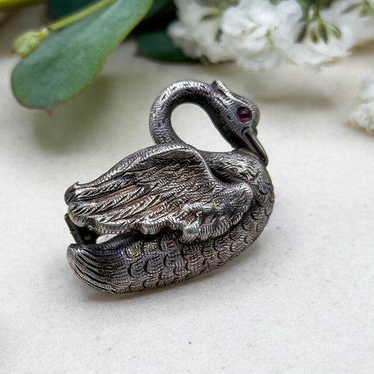 Silver swan figurine on a light surface with green leaves and white flowers in the background