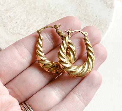 Both twisted gold hoops rested across a palm and fingers for scale, each about the length of a finger joint, with the hinged catch wires standing up at the top.