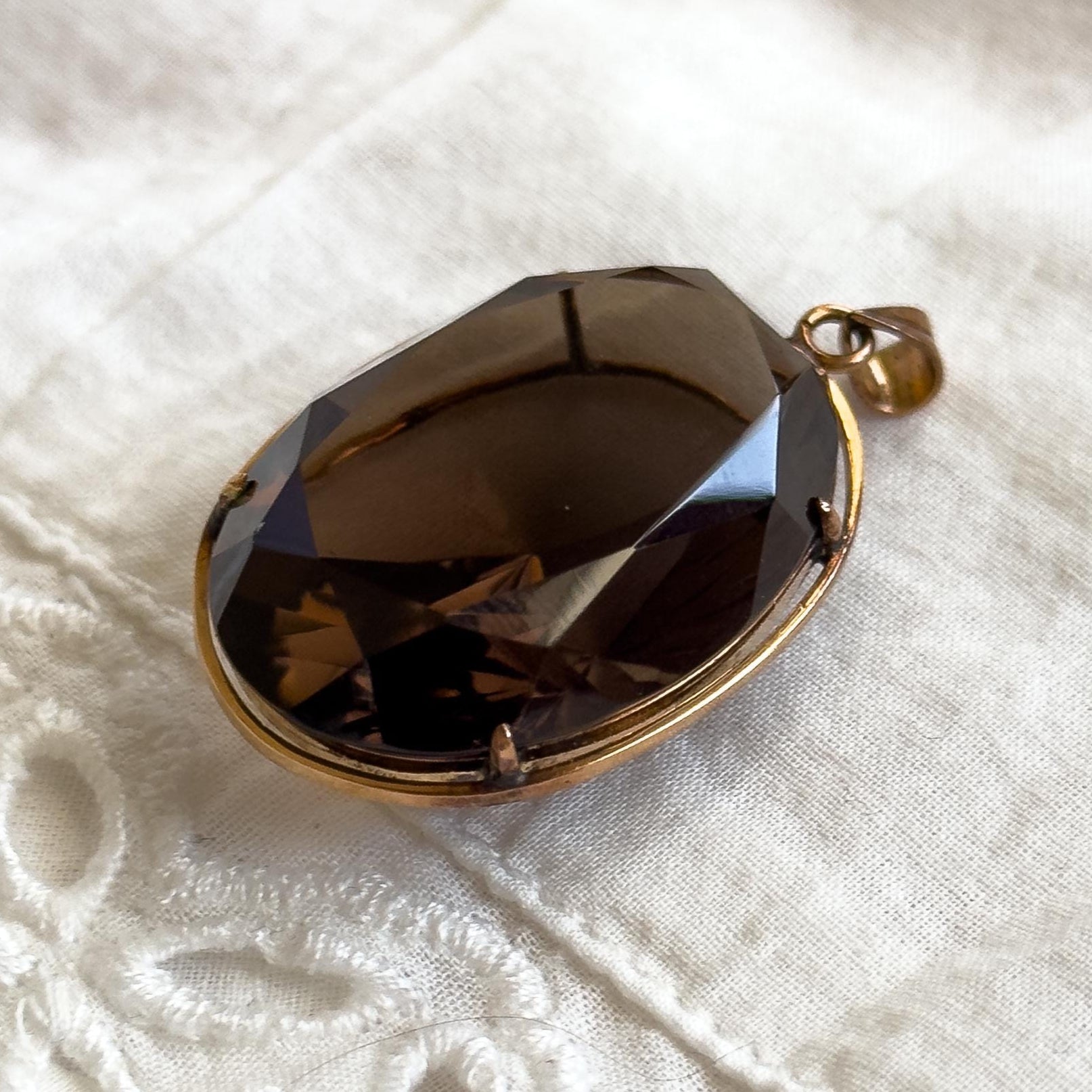 Brown teardrop pendant on a gold chain on a white textured fabric background