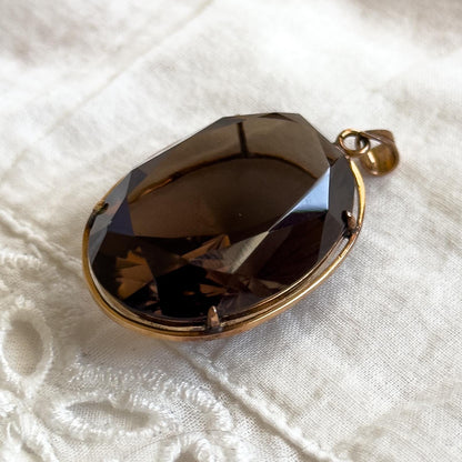 Brown teardrop pendant on a gold chain on a white textured fabric background
