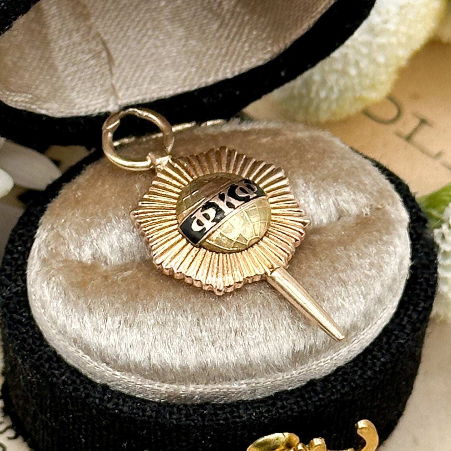 Gold key-shaped pendant with a sun design in a black jewelry box on a floral background