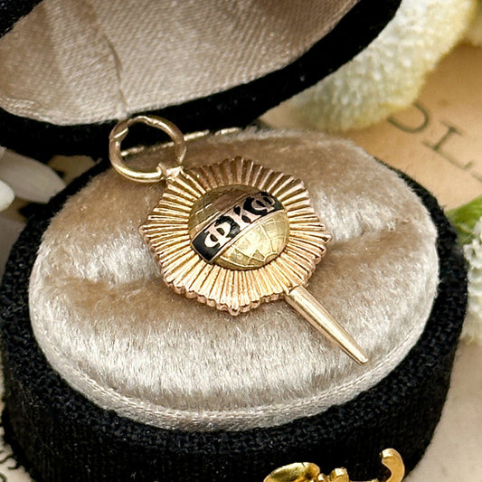 Gold key-shaped pendant with a sun design in a black jewelry box on a floral background