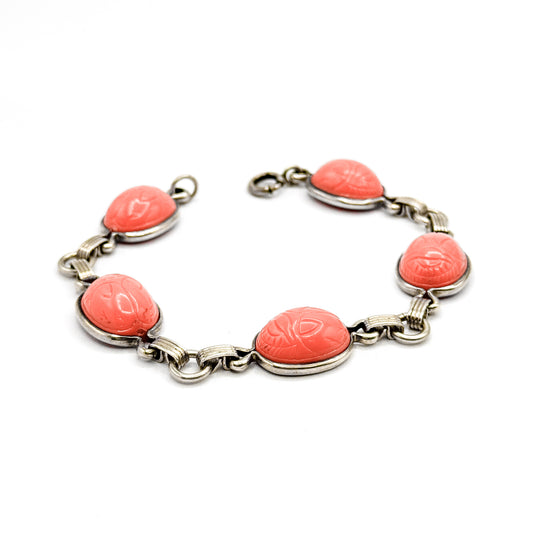 Vintage sterling silver bracelet with five coral-hued plastic scarab cabochons, laid in an open curve on a white background so the bezels, ribbed figure-eight links and spring ring clasp all show.