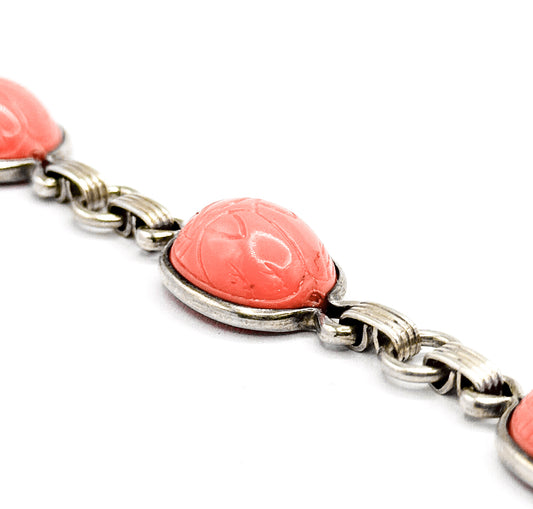 Close-up along the length of the bracelet, one coral-hued plastic scarab cabochon filling the frame in its sterling silver bezel between ribbed figure-eight links.