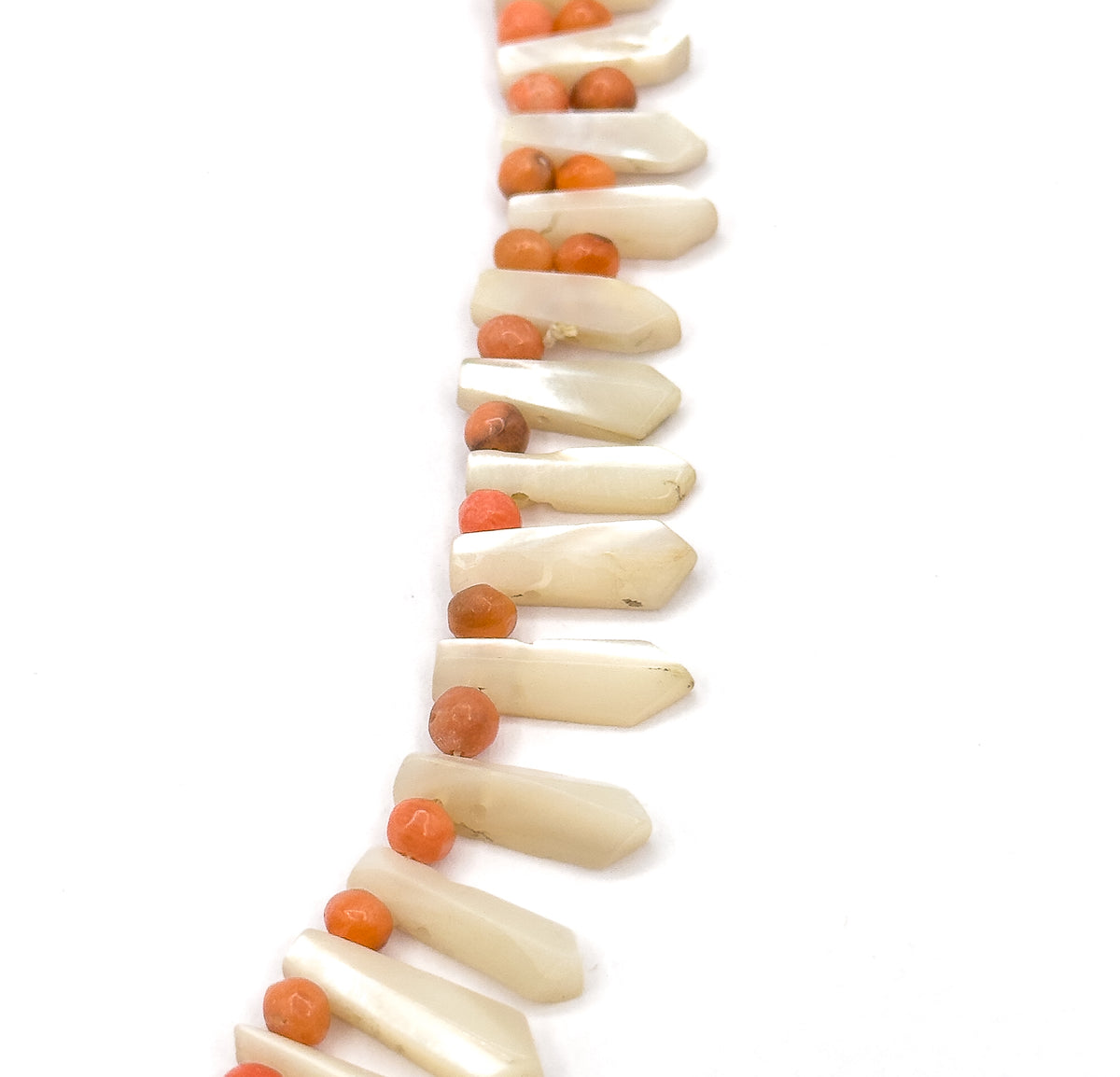 A near-vertical run of the strand down the plain white background, the pickets angling out to the right like a fringe while the coral beads line up along the left, largest drops at the lower centre.