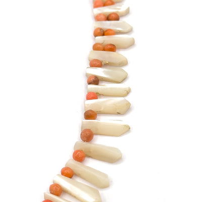 A near-vertical run of the strand down the plain white background, the pickets angling out to the right like a fringe while the coral beads line up along the left, largest drops at the lower centre.