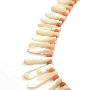 A close, shallow-focus side view where the milky pickets lie almost flat and overlapping like feathers, the coral beads glimpsed only in the gaps along the upper edge as the strand curves away.