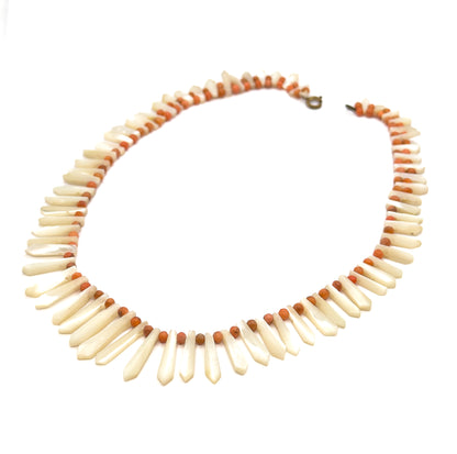The whole necklace laid out as an open oval on white, the full circuit visible at once with the clasp at the top and the pickets lengthening steadily toward the bottom centre.