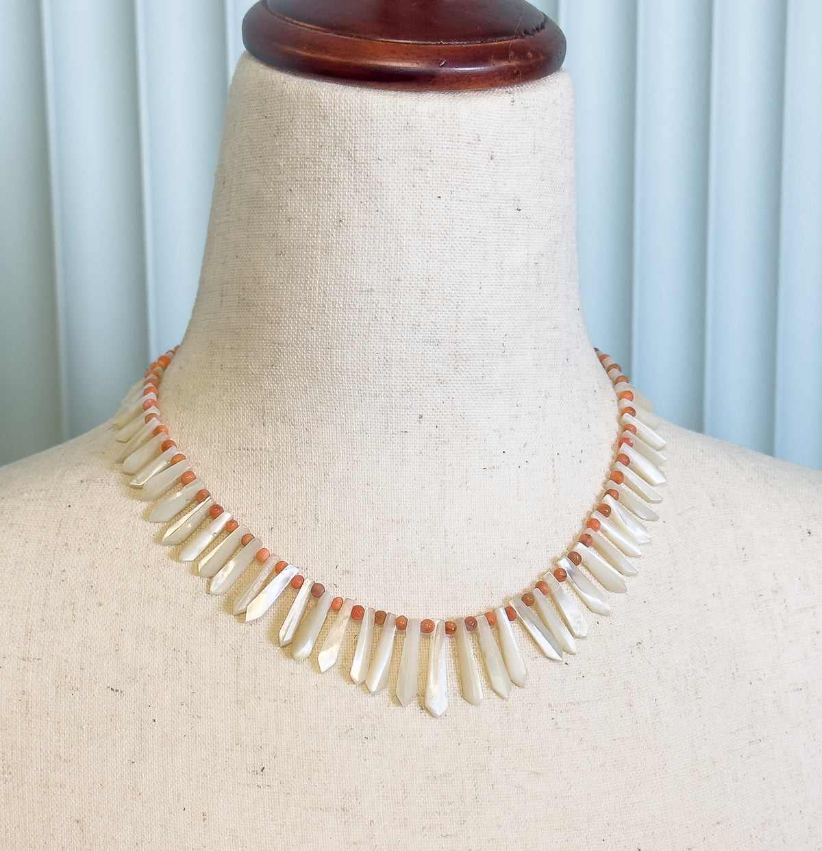 Closer view of the same dress form, showing how the drops lengthen toward the centre front while the small orange beads sit between them along the cord.