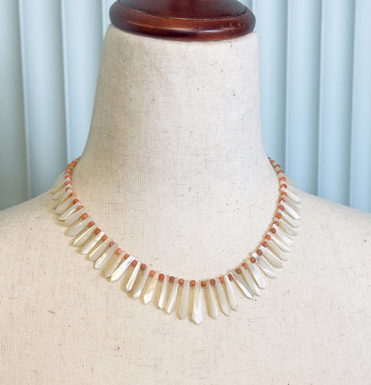Closer view of the same dress form, showing how the drops lengthen toward the centre front while the small orange beads sit between them along the cord.